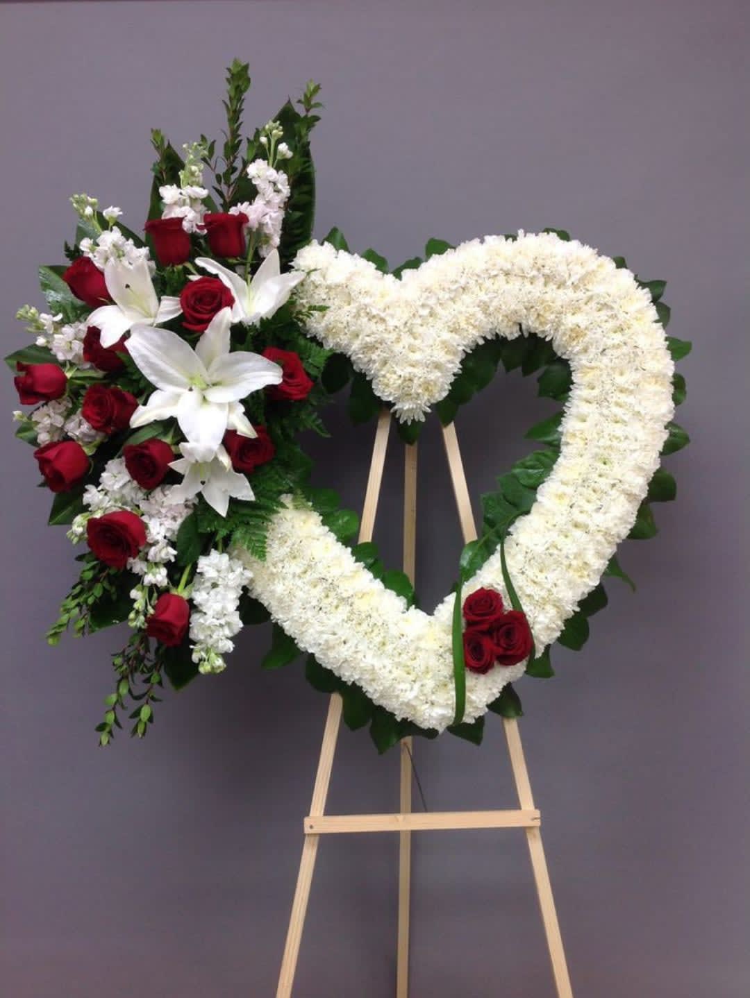 Heart-shaped floral wreath with red roses and white lilies on an easel