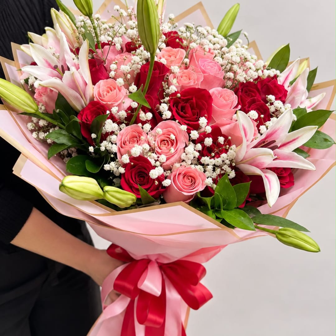 Bouquet of pink and red roses with white lilies wrapped in pink paper