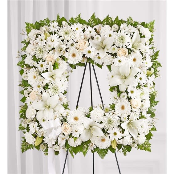 White floral wreath on a black easel with lilies and daisies