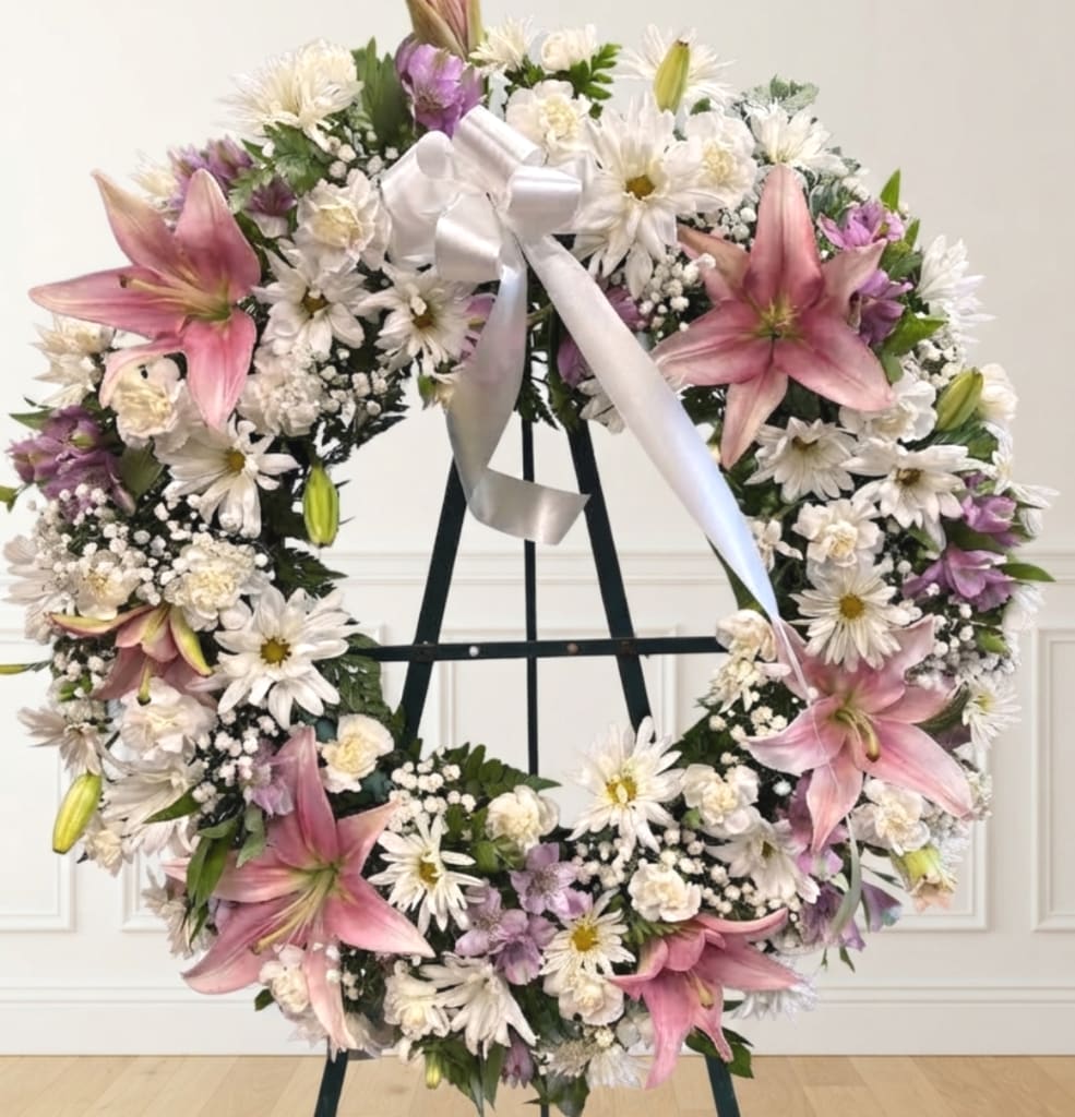 Large floral wreath with pink lilies, white daisies, and a white ribbon on an easel