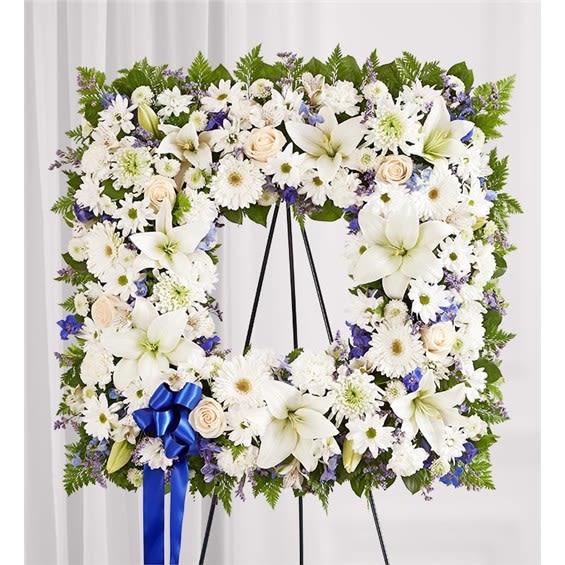Large white floral wreath on a black stand with a blue ribbon