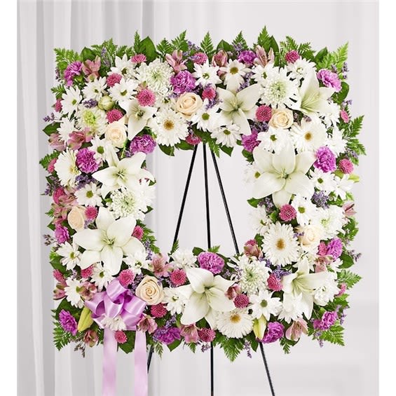 Square floral wreath with white lilies, daisies, and pink blooms on an easel
