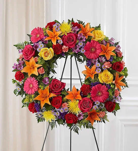 Heart-shaped floral wreath with roses, lilies, and daisies on a stand