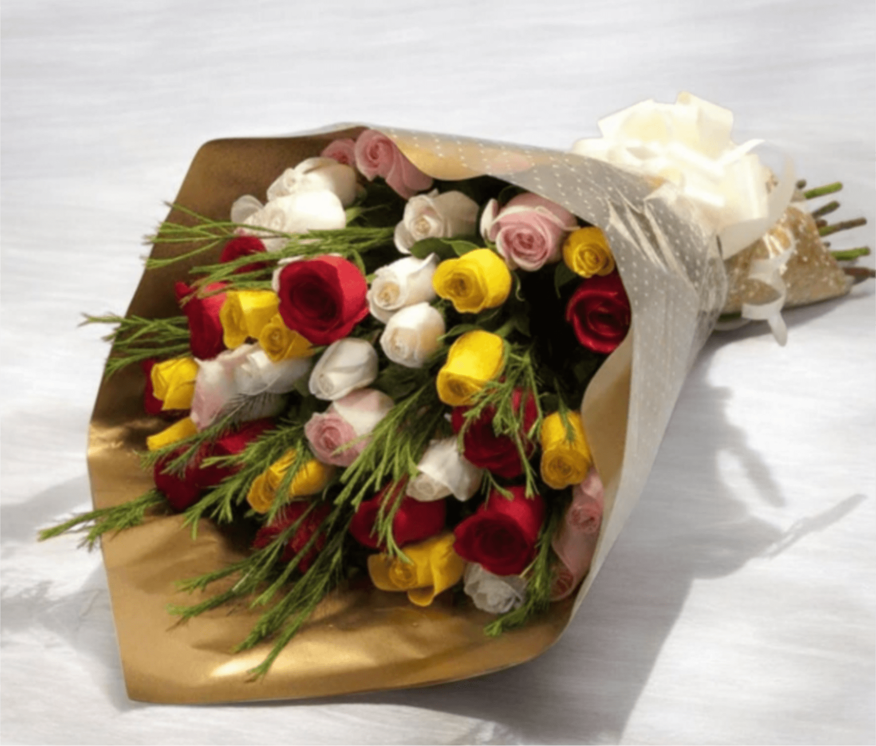 Bouquet off Mix Roses . - A vibrant mix of red, yellow, white and blush-pink roses creates an immediate impression of joyful romance - the perfect birthday bouquet, anniversary roses, or bright "thinking of you" gift. Arranged in a rounded, hand-tied style, the compact cluster reads classic and abundant while the varied color palette keeps the feeling playful and celebratory for congratulations or Valentine's Day.  Long, feathery greenery is woven through the blooms to add texture and movement against the dense rose heads, giving the bouquet a slightly garden-style, airy finish. The stems are dressed in metallic gold wrapping paper with a sheer, dotted or translucent white overlay and finished with a white decorative ribbon and tissue-a polished presentation that arrives ready to gift. This arrangement is sized to feel generous without overwhelming; to keep it looking fresh, recut stems at an angle and change the water every two days after delivery.