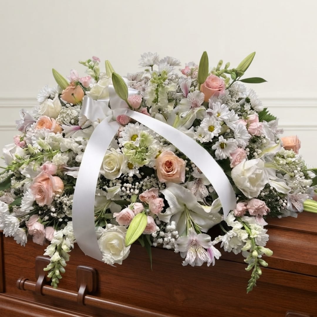 Pastel floral casket spray with white ribbon on a wooden coffin