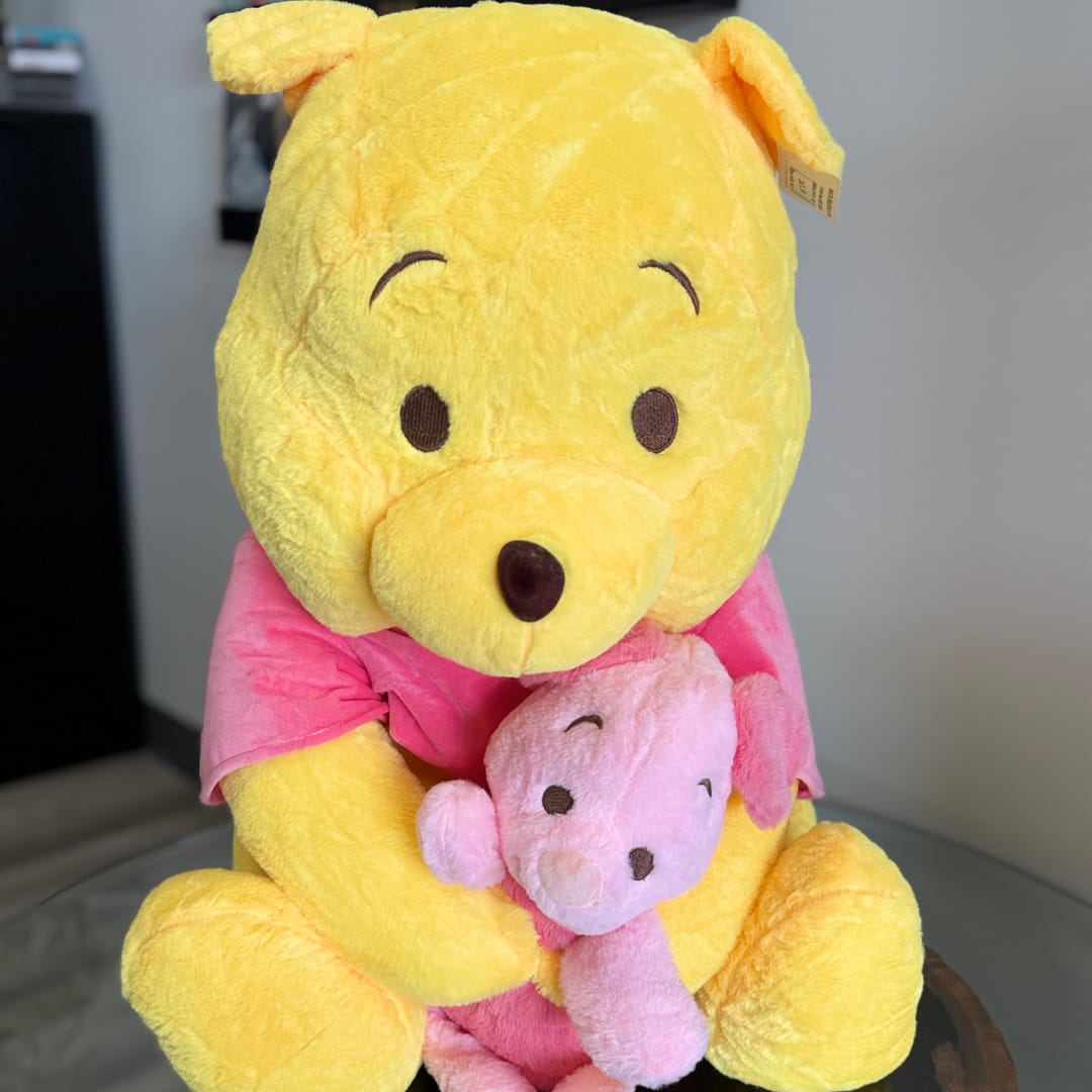 Yellow Winnie the Pooh plush holding a pink Piglet plush
