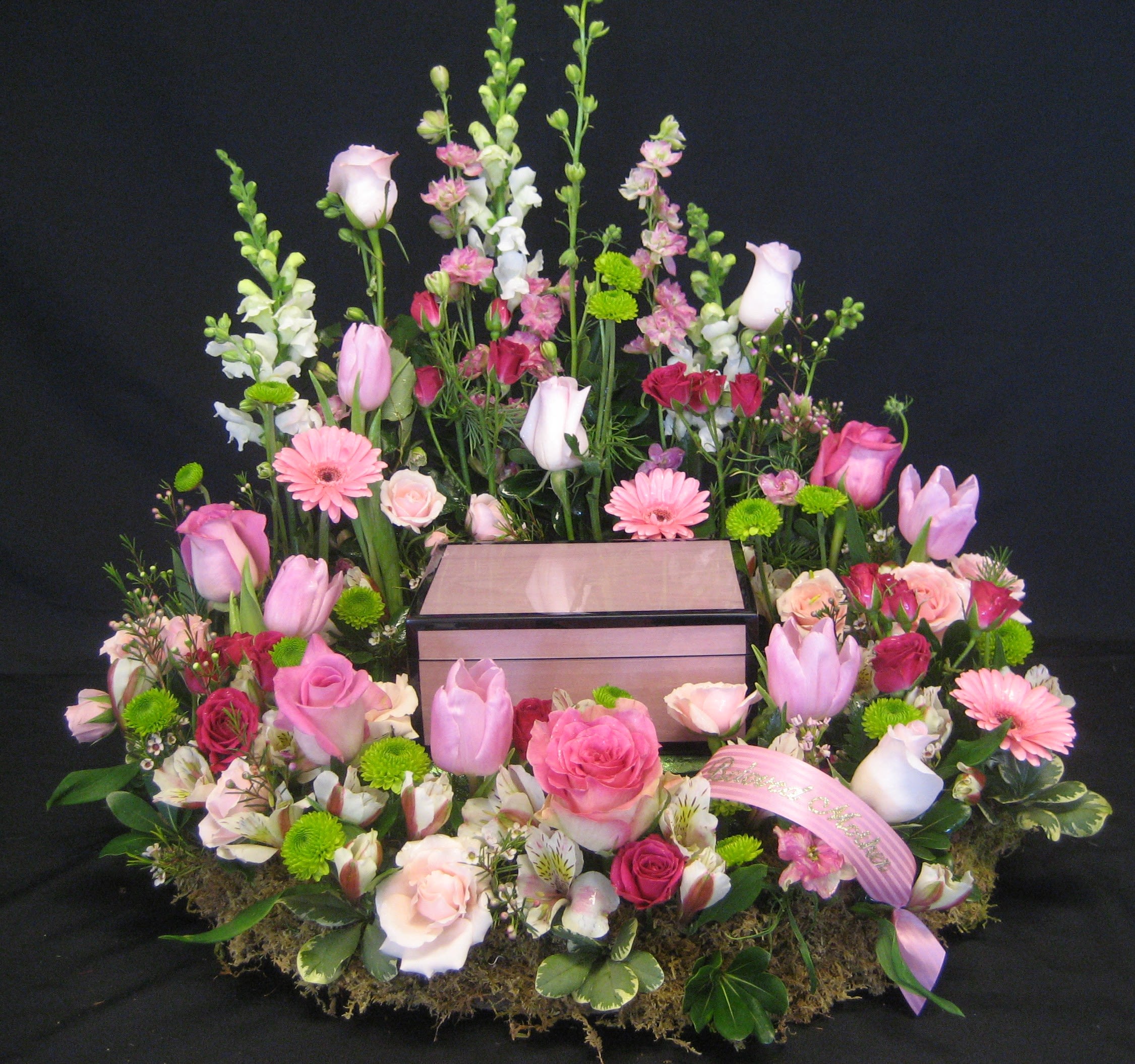 Pink and white floral arrangement surrounding a wooden box on a black background