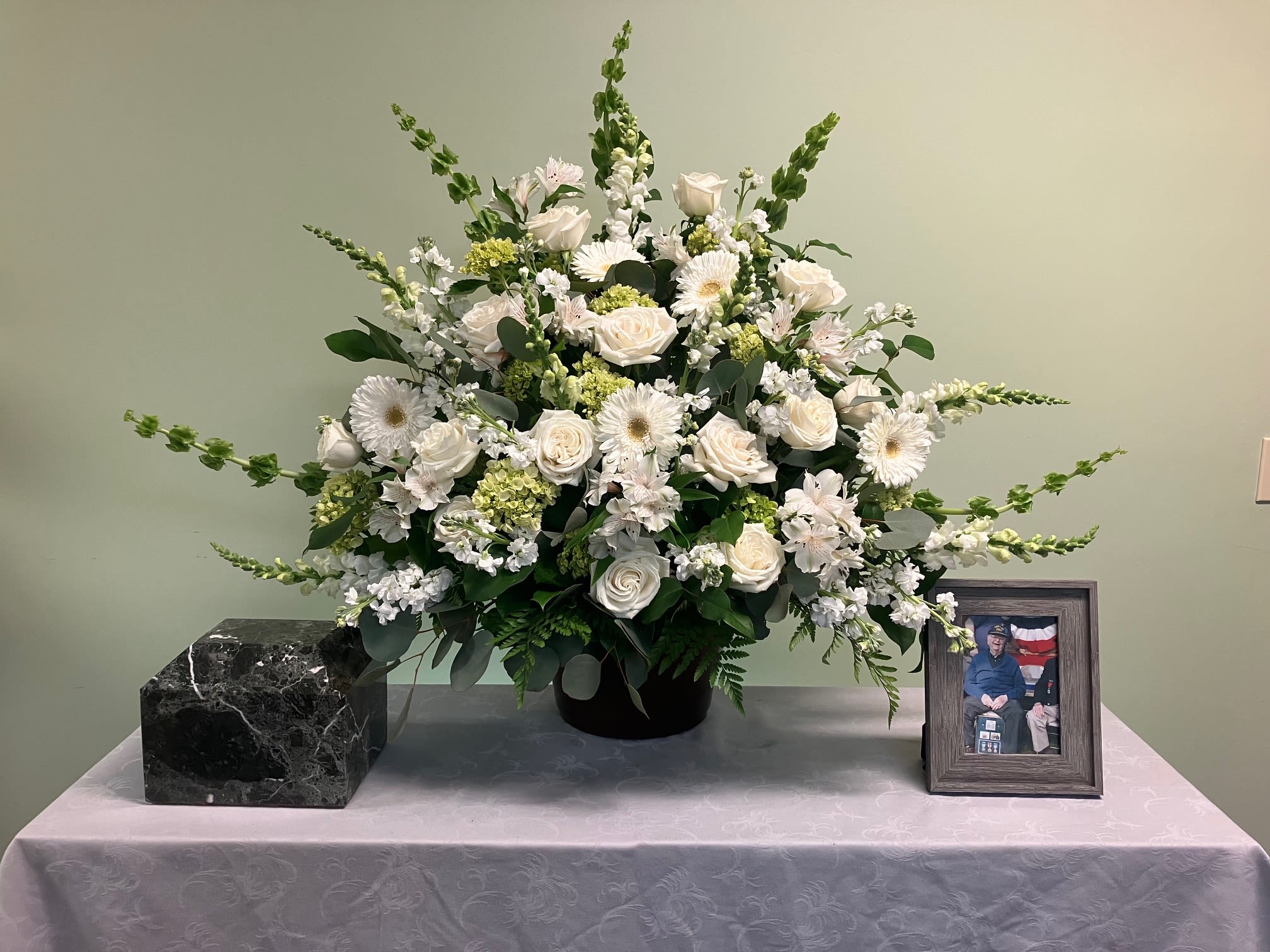 White floral arrangement in a black vase on a table with a framed photo