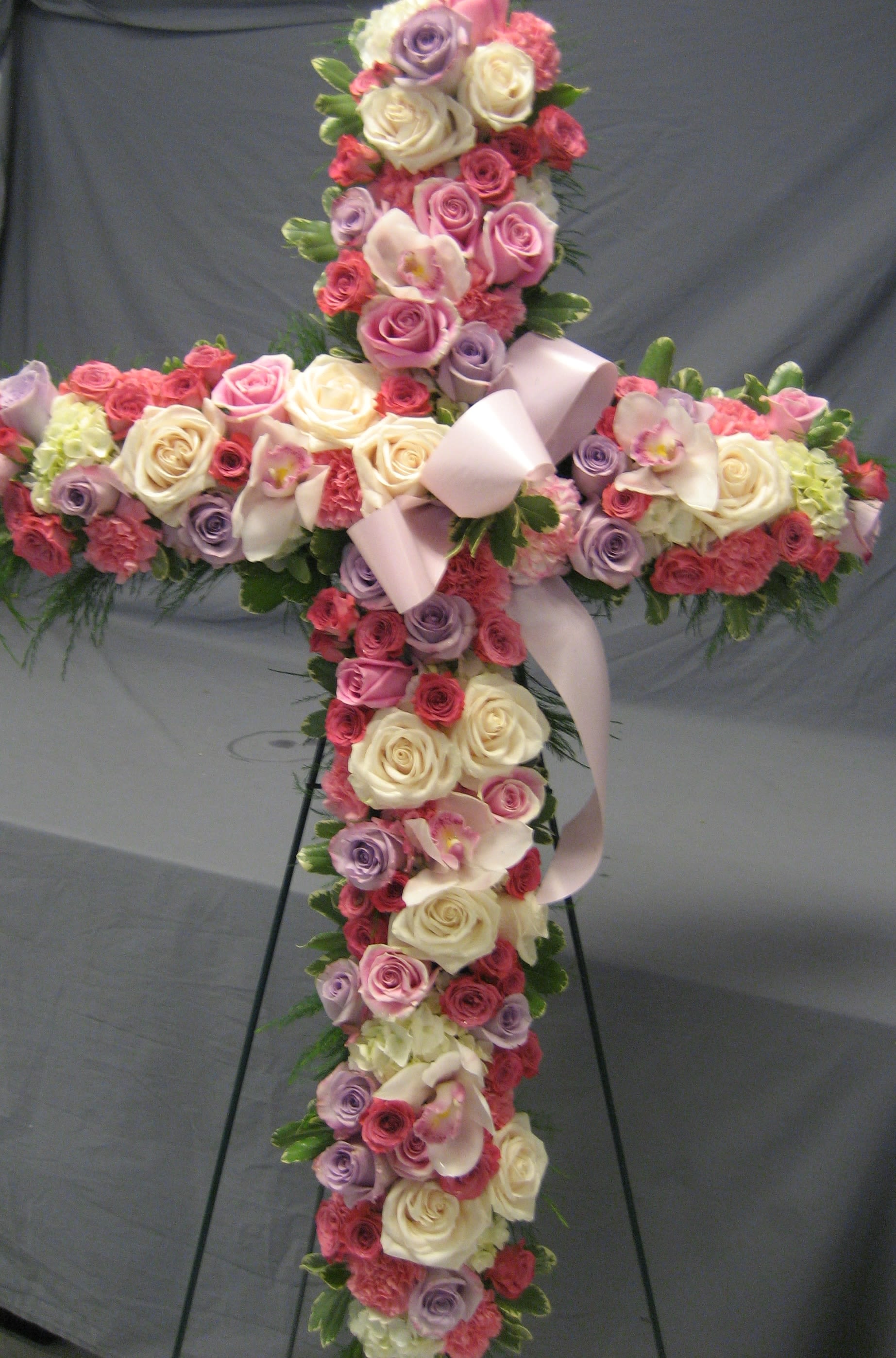Cross-shaped floral arrangement with roses and orchids on a stand