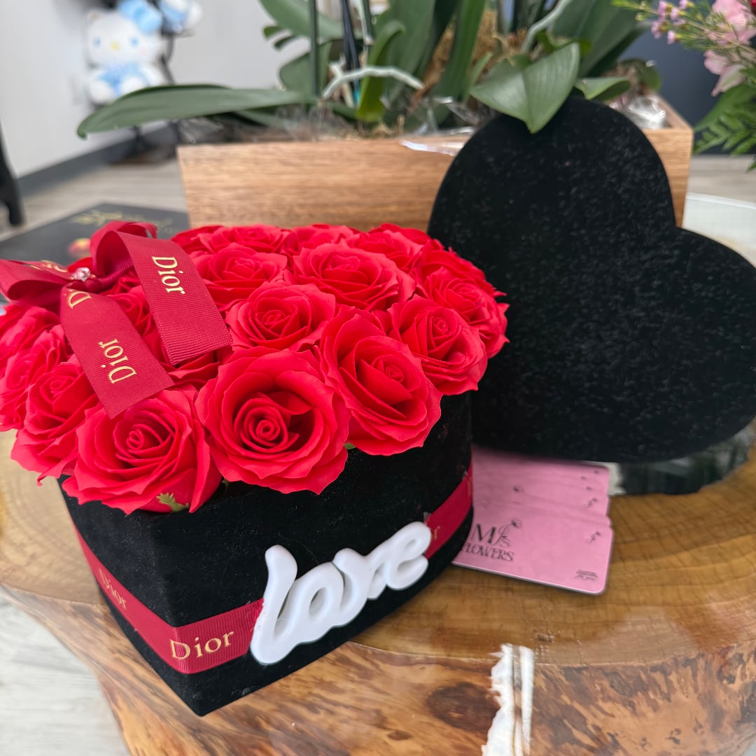 Red roses arranged in a black heart-shaped box with a white "love" decoration