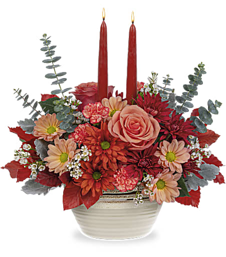 Red and peach floral arrangement with two red taper candles in a white bowl