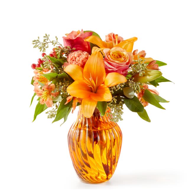 Orange and pink mixed flowers arranged in an amber glass vase