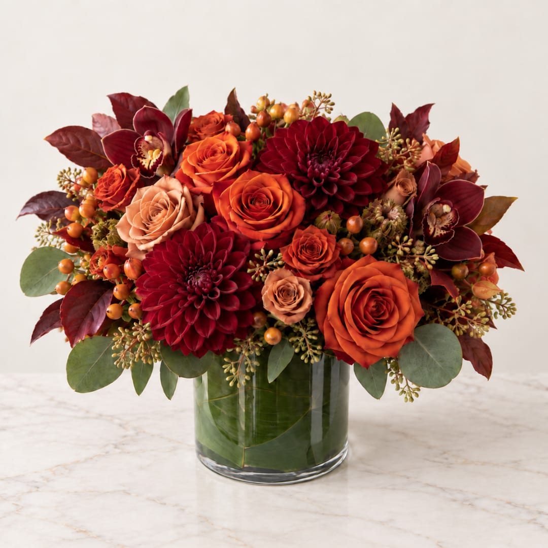Orange and burgundy flower arrangement in a glass vase