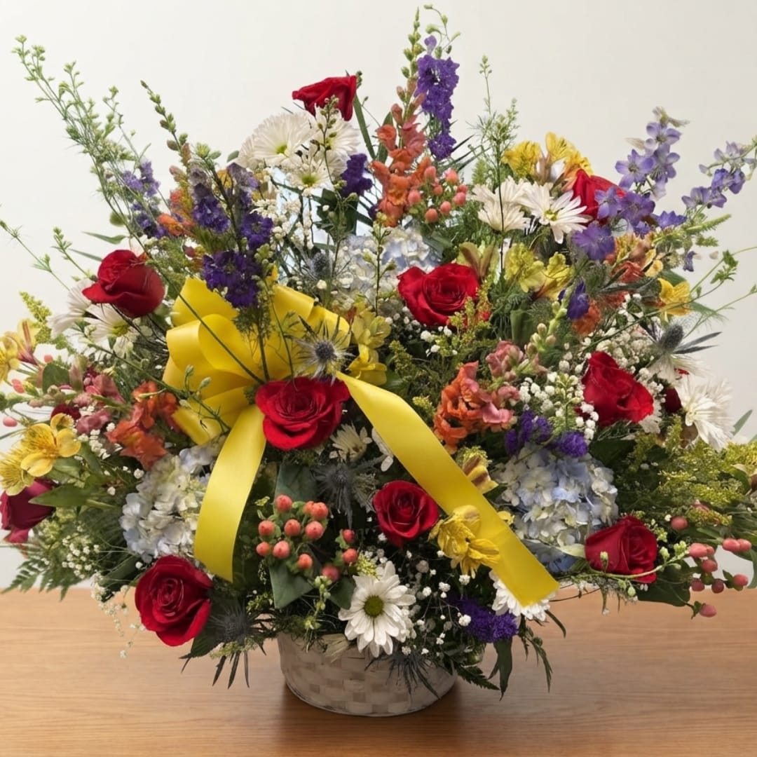 Mixed bouquet of red roses, white daisies, and purple flowers in a basket with a yellow ribbon