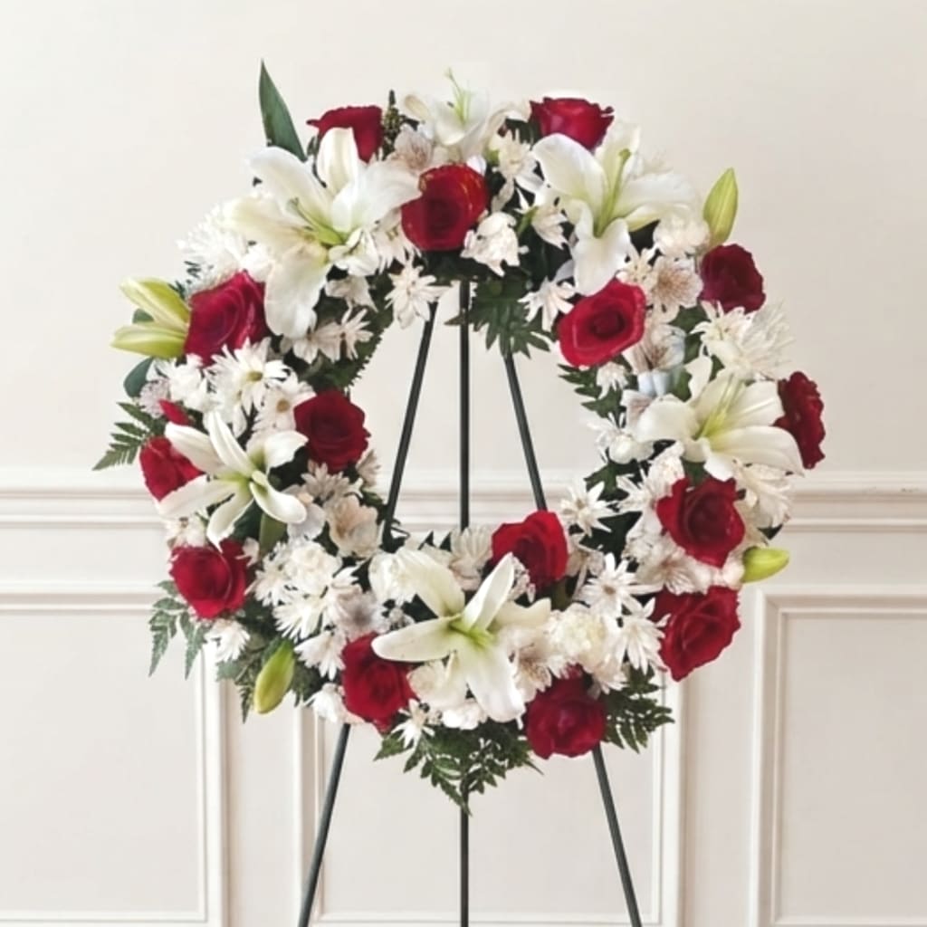 Red roses and white lilies arranged in a wreath on a black stand