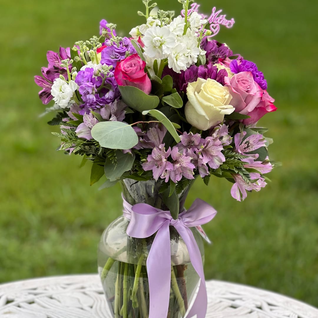 Mixed bouquet of roses and purple flowers in a glass vase with a lavender ribbon