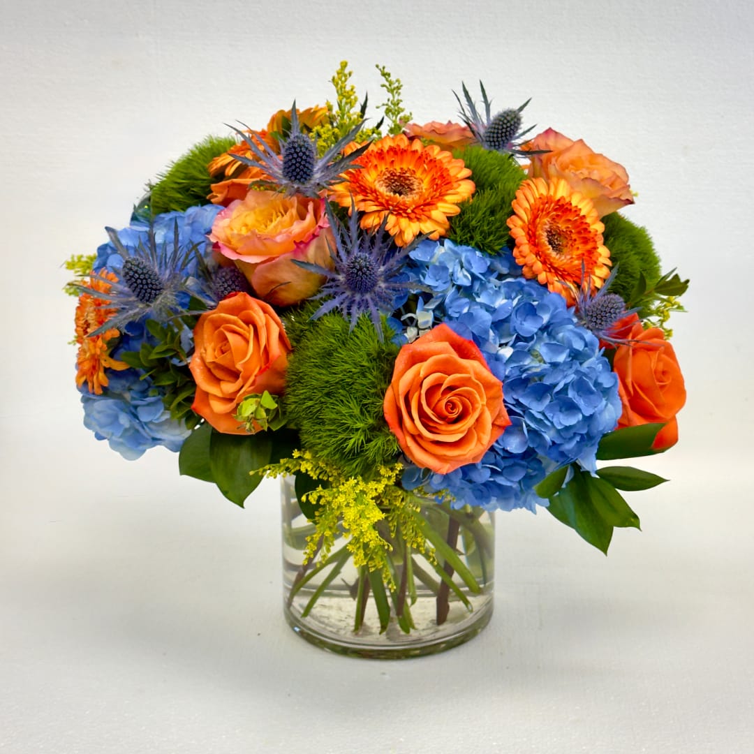 Orange roses and blue hydrangeas in a clear glass vase