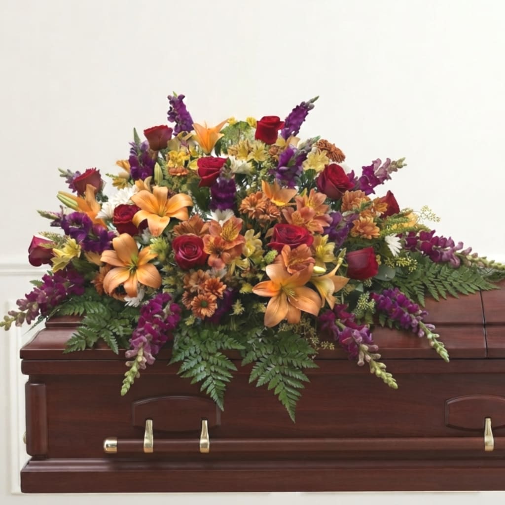 Colorful floral spray on a wooden casket with roses and lilies