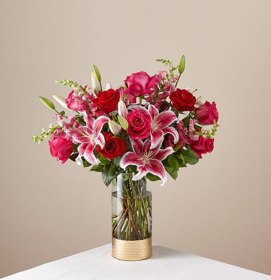 Pink and red roses with lilies in a clear glass vase