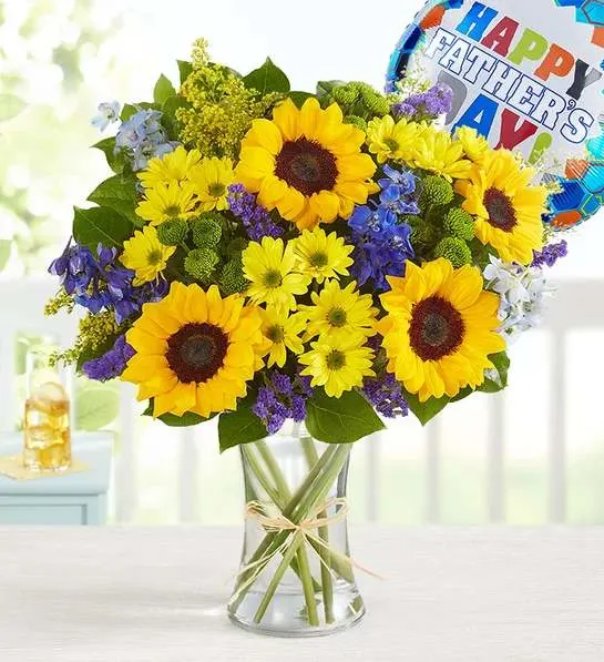 Bouquet of sunflowers, yellow daisies, and purple flowers in a glass vase