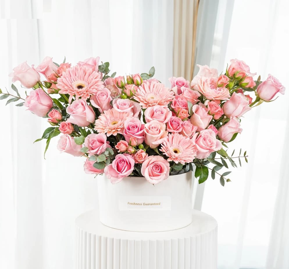 Pink roses and gerbera daisies arranged in a white hatbox