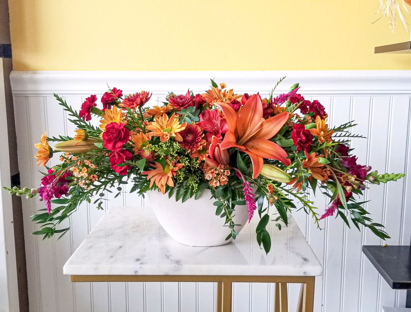 Long floral arrangement in a white bowl with orange lilies and red-orange blooms