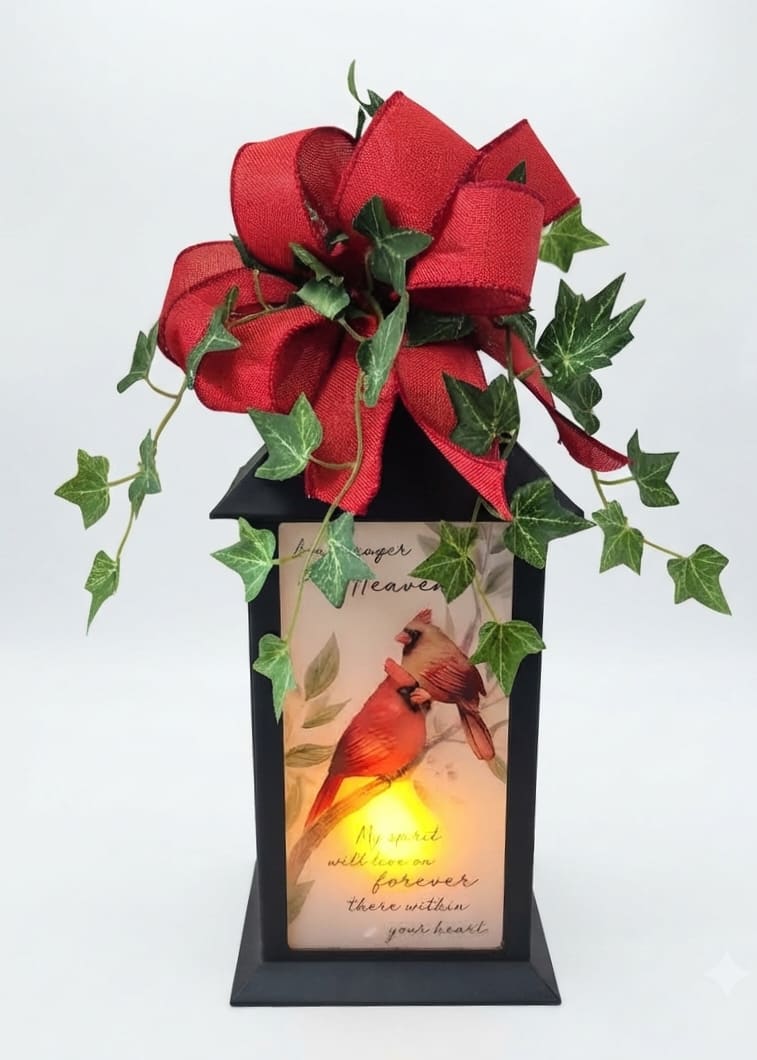 Black lantern with a red bow and ivy, featuring a lit cardinal memorial panel.