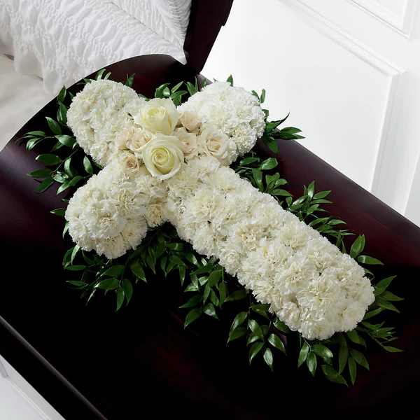 Peaceful Memories Casket Spray Cross  - The Peaceful Memories Casket Spray is a gorgeous way to commemorate the faith and devotion of the deceased. White carnations are arranged in the shape of a cross accented in the middle with white roses and spray roses and along the sides with lush greens to create a lovely casket spray that brings peace and solace to those that attend their final farewell.