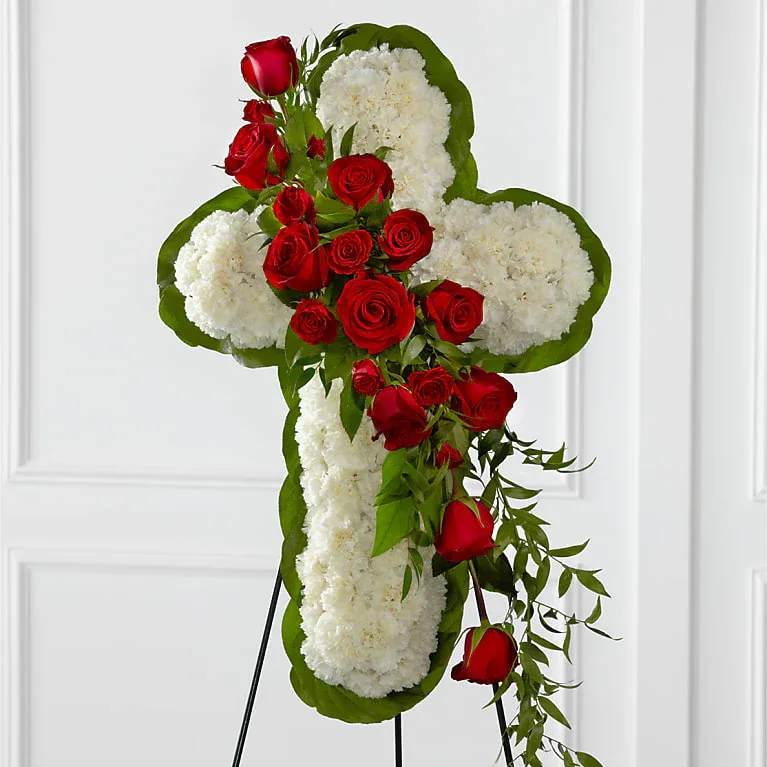 Cross-shaped floral tribute with red roses and white flowers on a stand