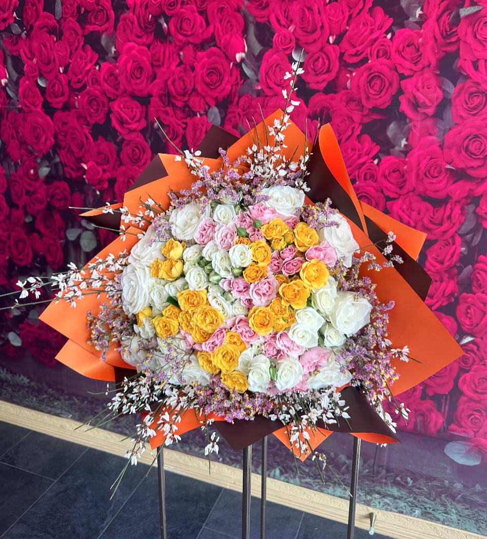 Large bouquet of white, pink, and yellow roses with orange wrapping