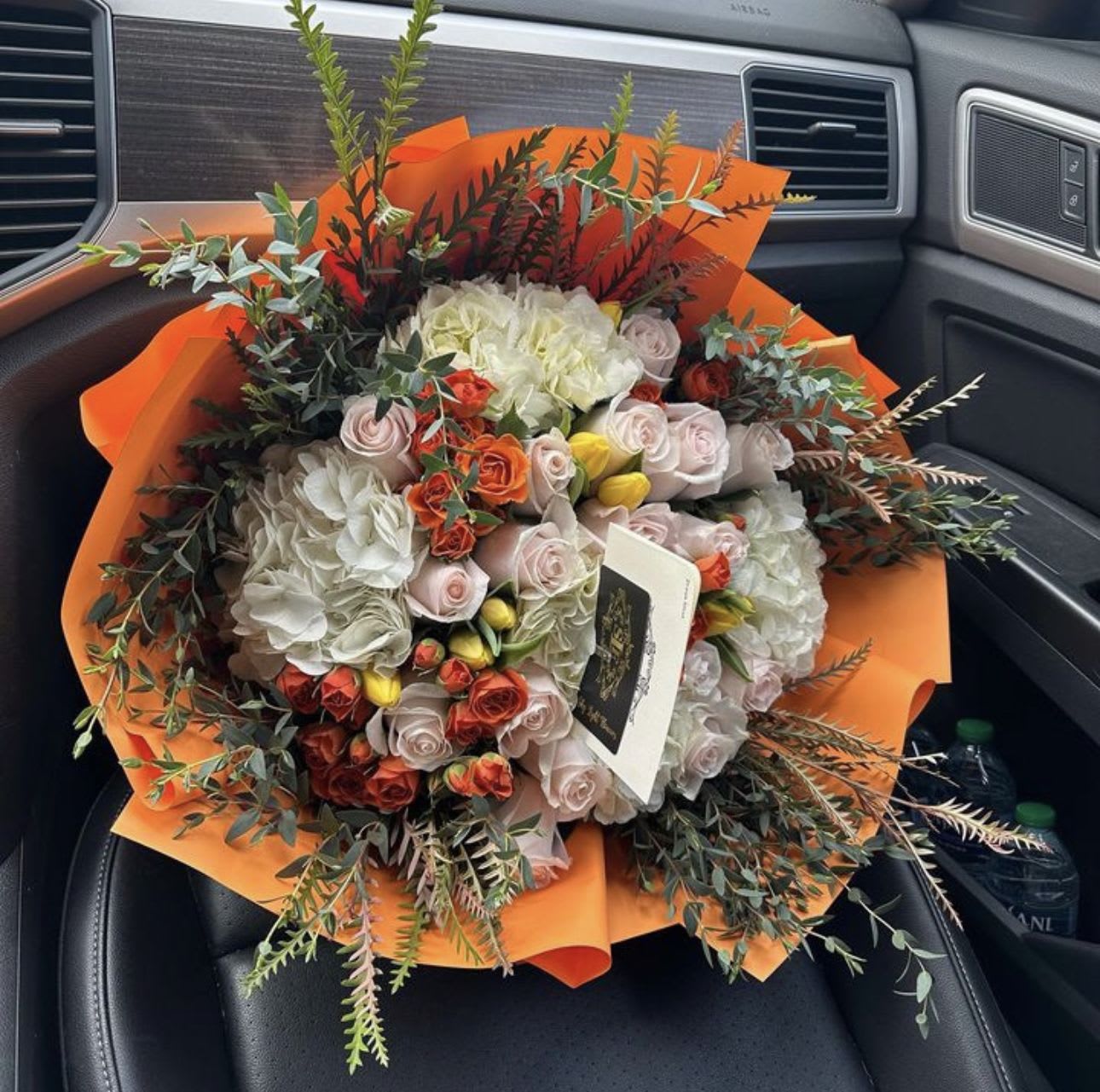 Mixed bouquet of roses and hydrangeas wrapped in bright orange paper