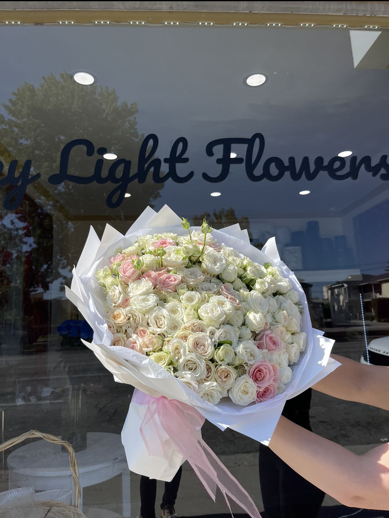 Large bouquet of white and blush roses wrapped in white paper with a pink ribbon