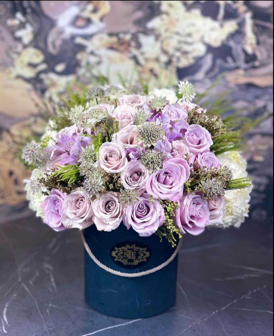 Lavender roses and white filler flowers in a blue hatbox