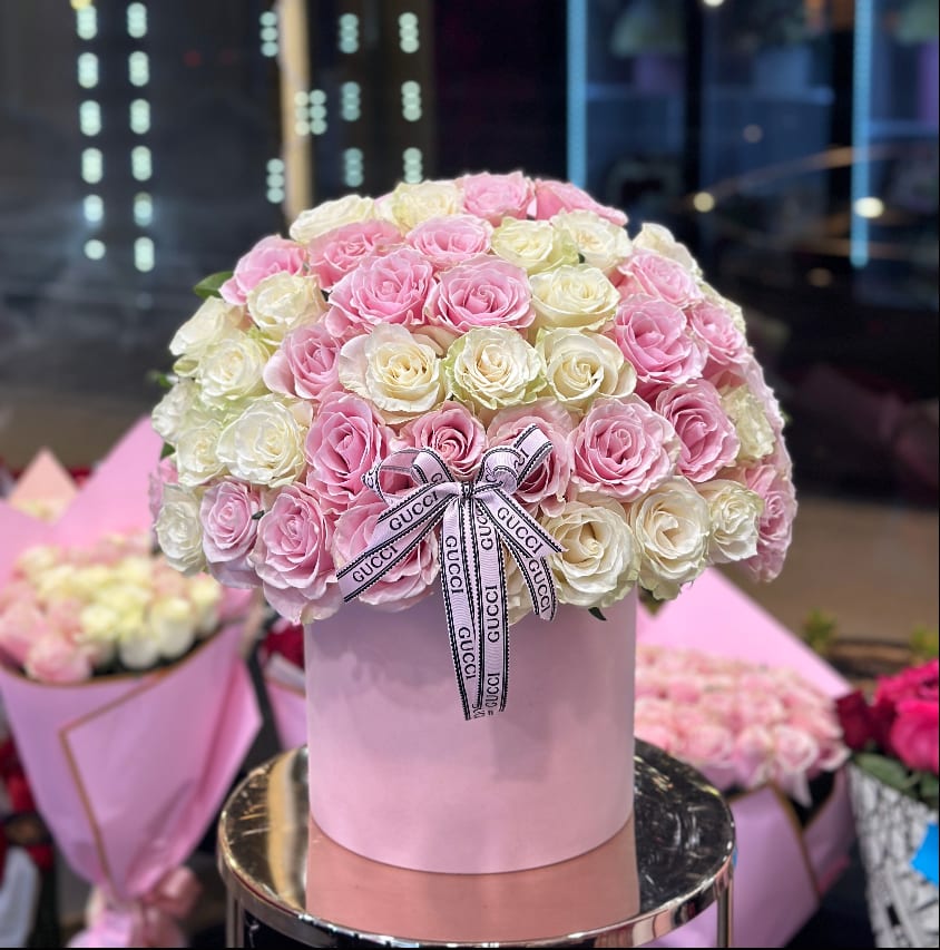Pink and white roses arranged in a round hatbox with a ribbon bow