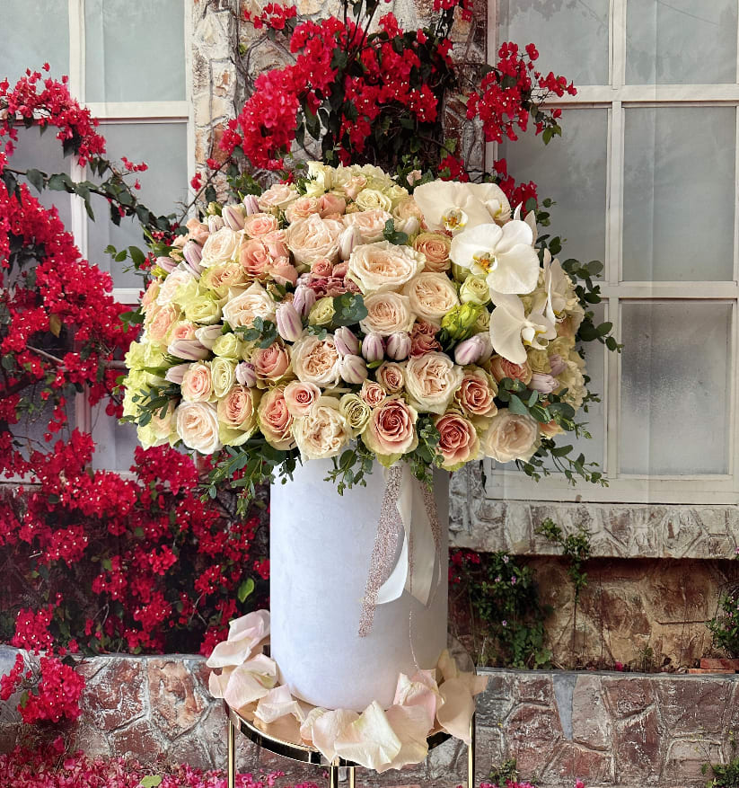 Large pastel rose arrangement with white orchids in a tall white vase