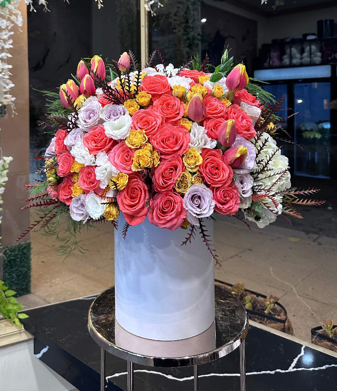 Large bouquet of pink, white, and yellow roses in a tall white box