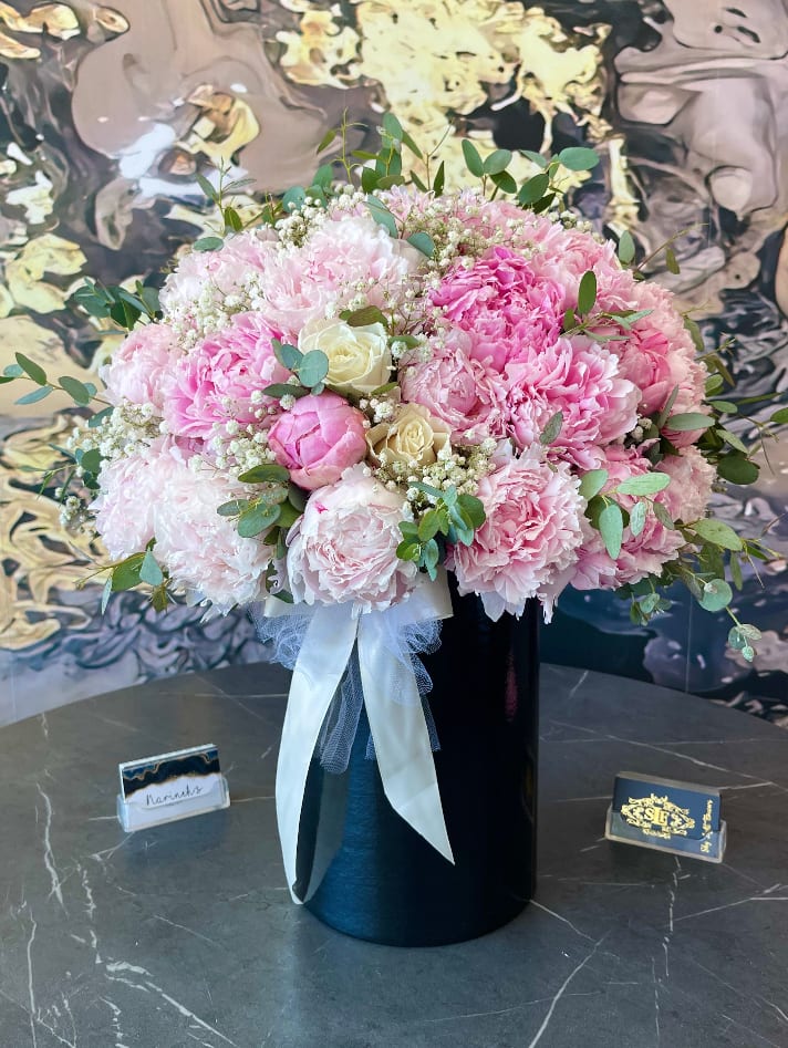 Pink peony and rose bouquet in a black vase with white ribbon