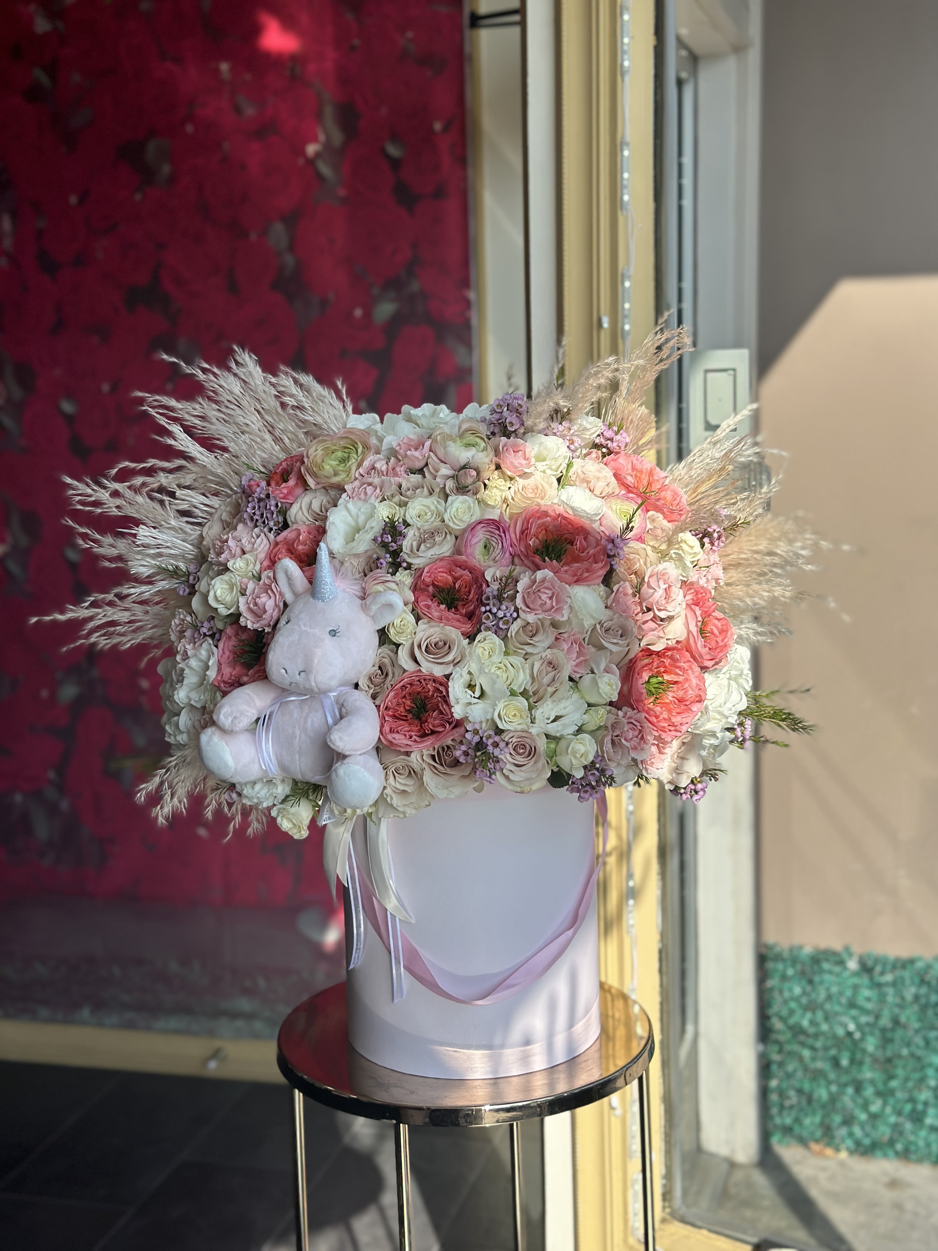 Pastel flower arrangement in a white hatbox with a plush unicorn