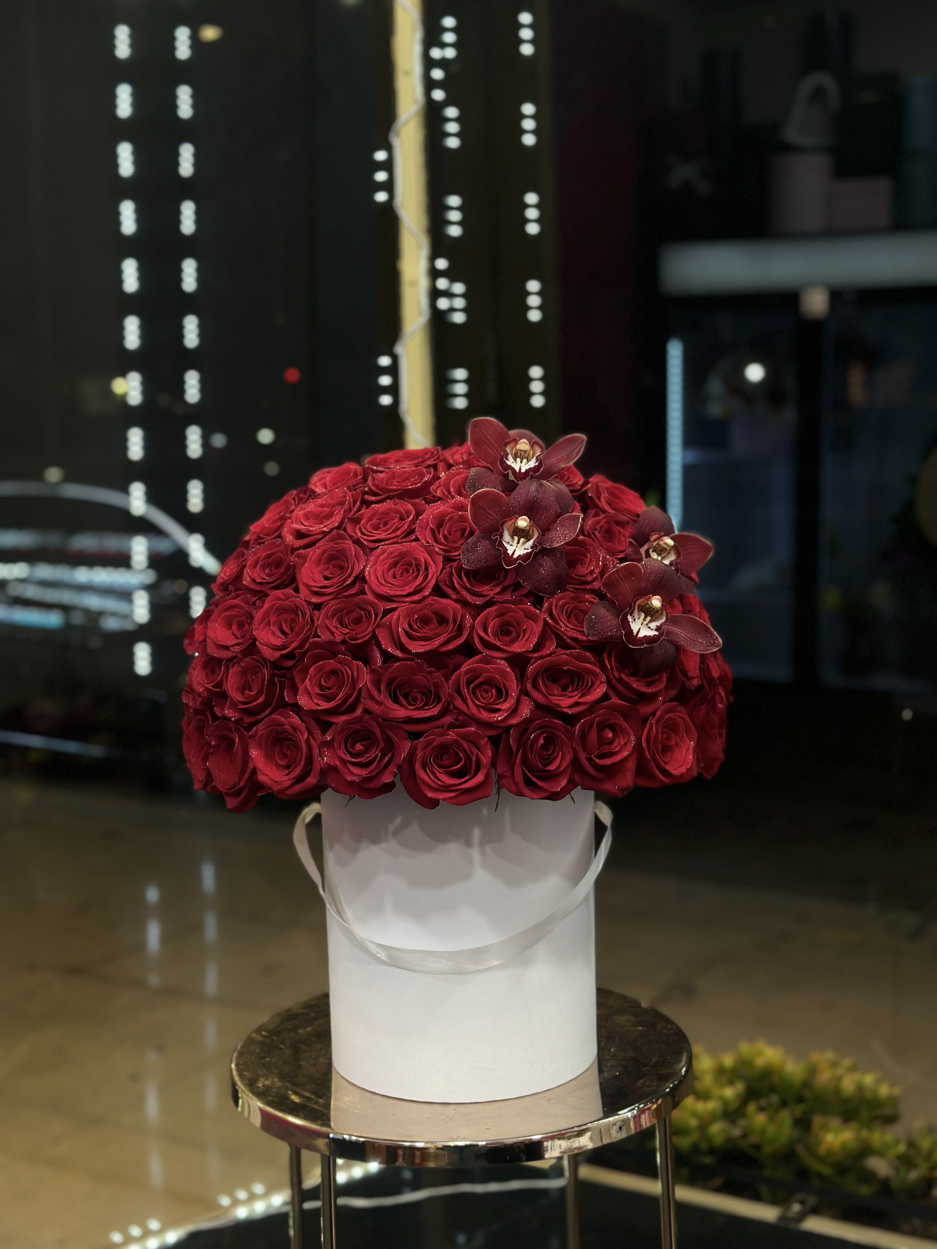 Red rose arrangement in a white hatbox with dark orchids