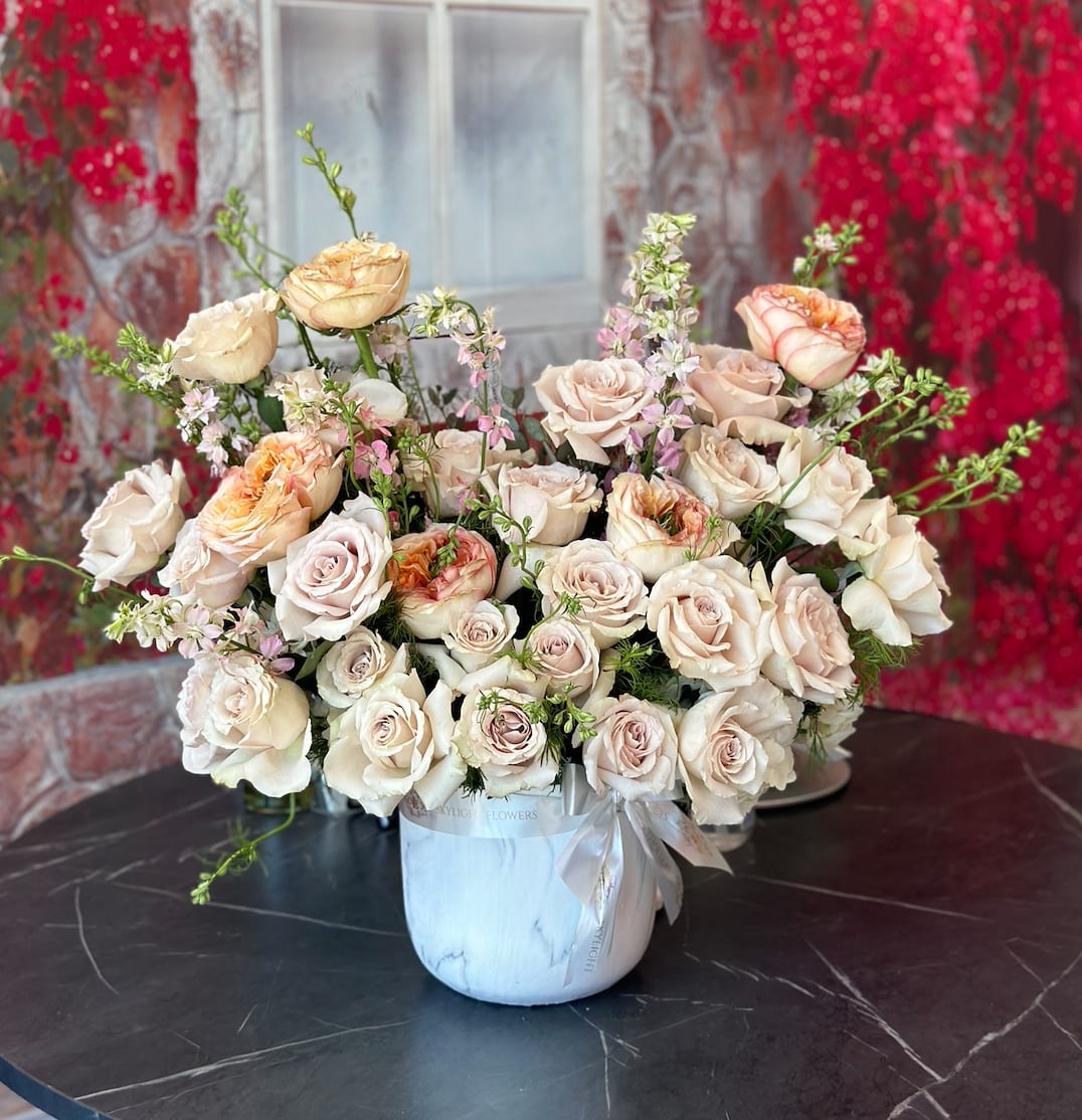 Cream and blush roses arranged in a white vase with a ribbon