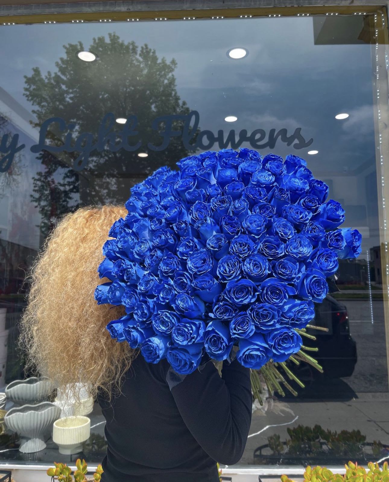 Large bouquet of vivid blue roses held in front of a shop window