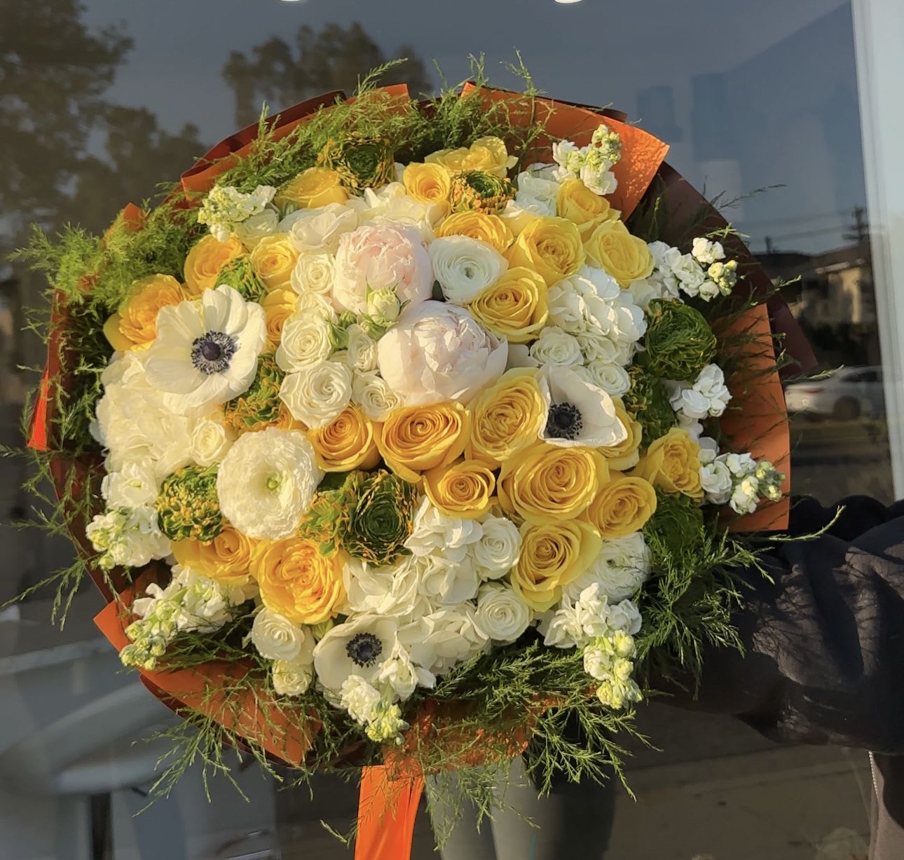 Large bouquet of yellow and white flowers wrapped in orange paper