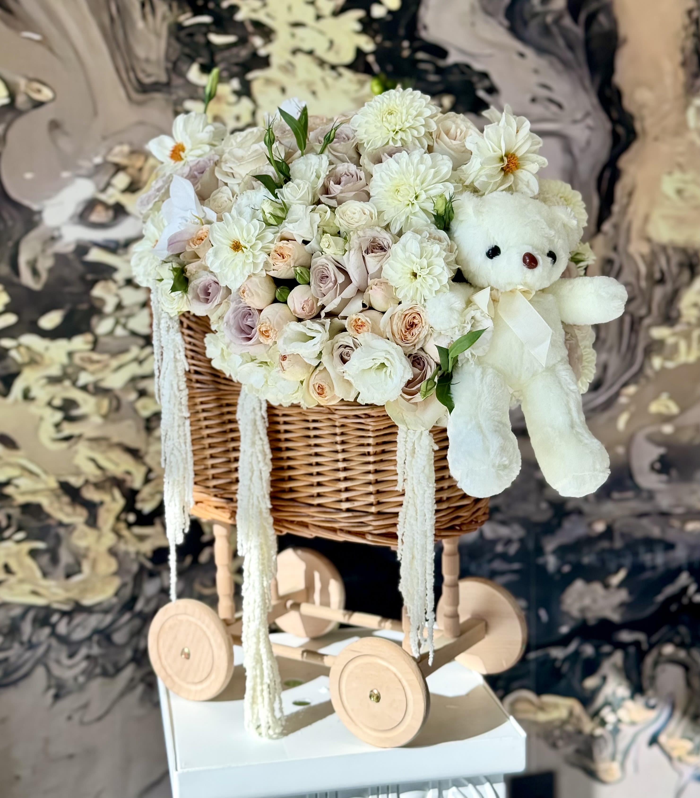 White floral basket arrangement with a teddy bear on a wooden cart