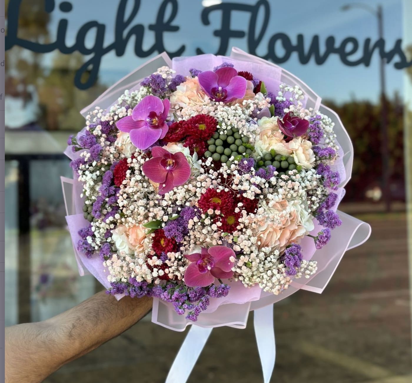 Large bouquet of pink orchids, red blooms, and purple filler flowers wrapped in pastel paper