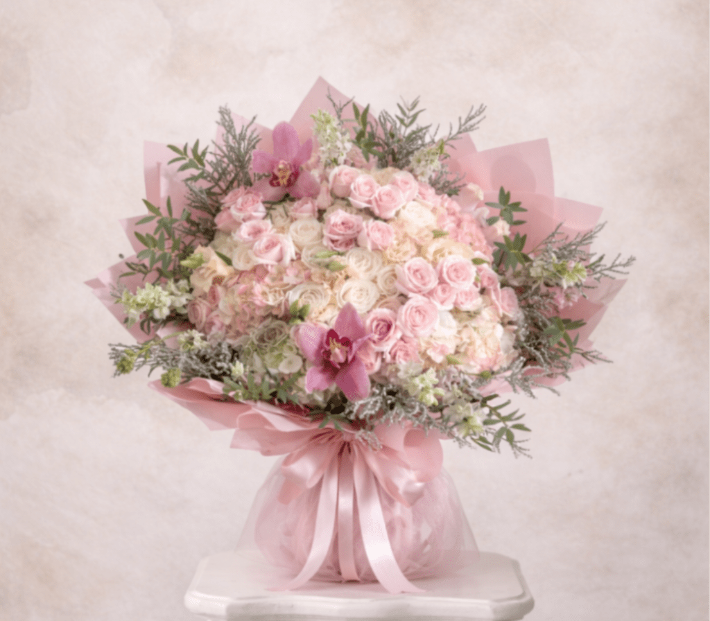 Large round bouquet of pale pink and white roses and hydrangeas with pink orchids, wrapped in pink paper and ribbon