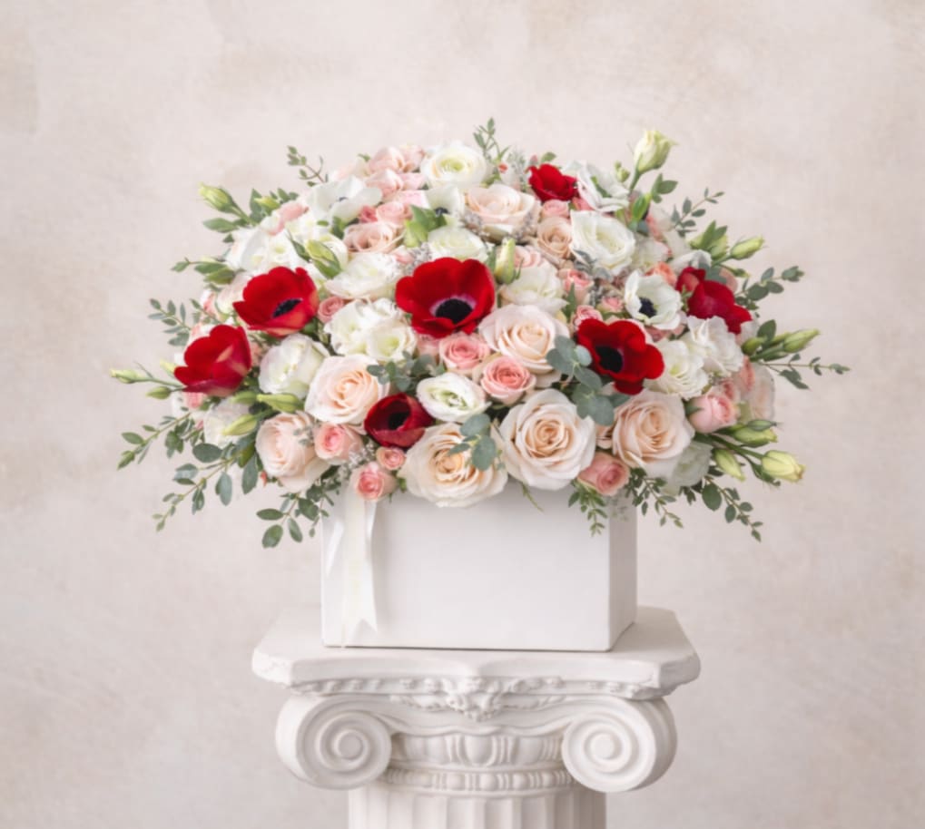 Bouquet of pale roses and red anemones in a white box