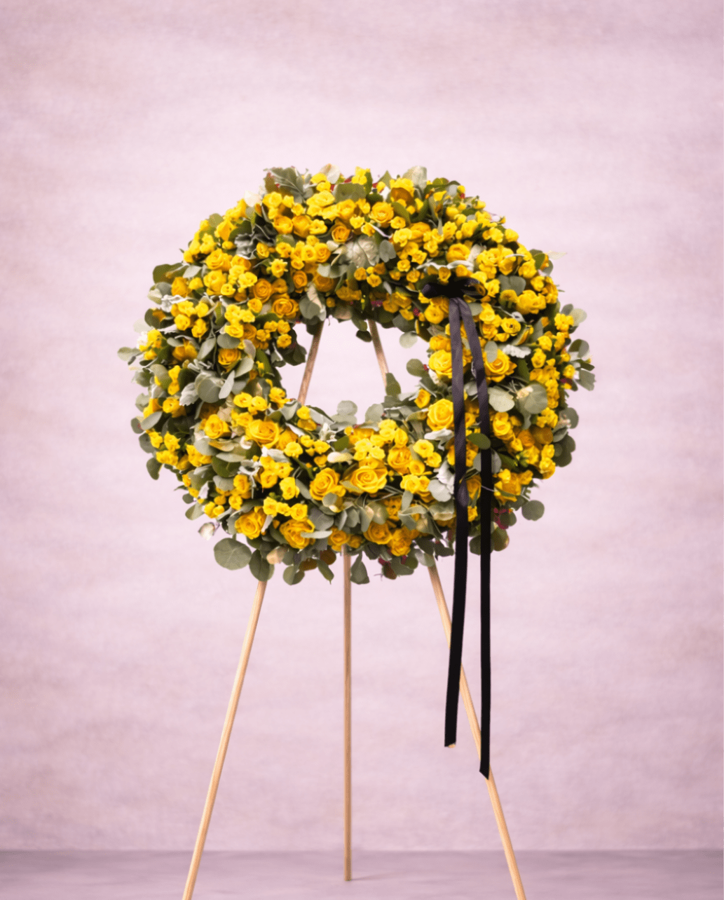 Large yellow rose wreath with black ribbon on a wooden easel stand