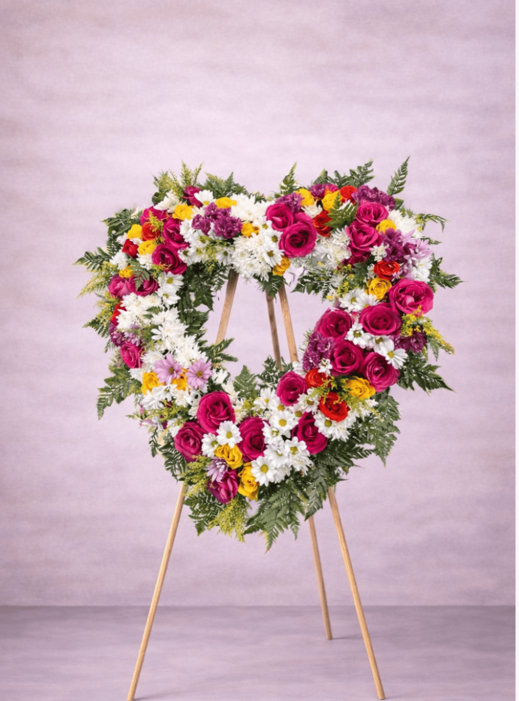 Heart-shaped standing wreath with pink and yellow roses and white daisies on a wooden easel