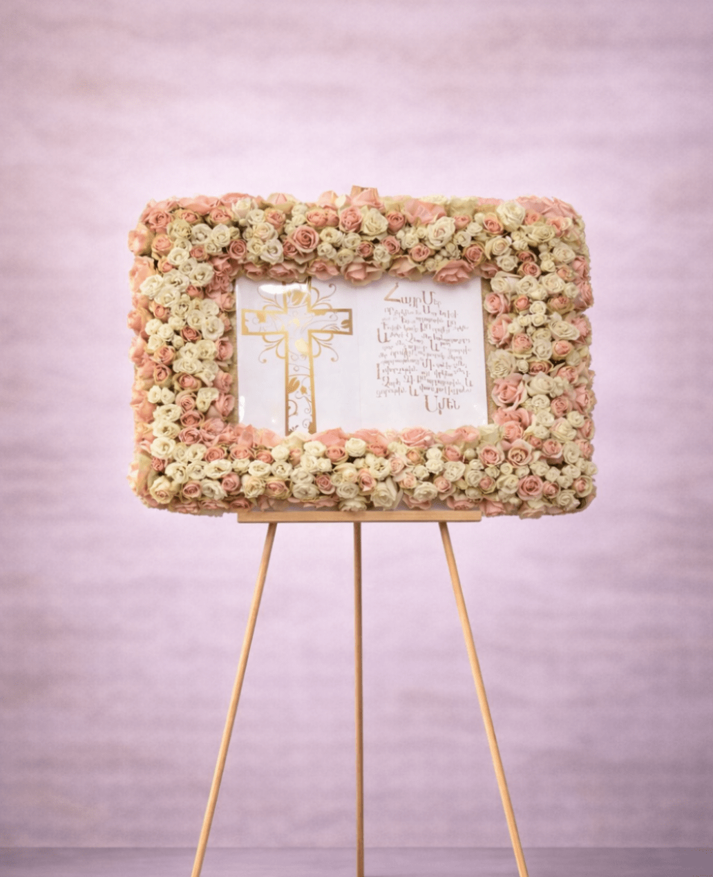 Rectangular frame of blush and cream roses around a printed cross panel on an easel.