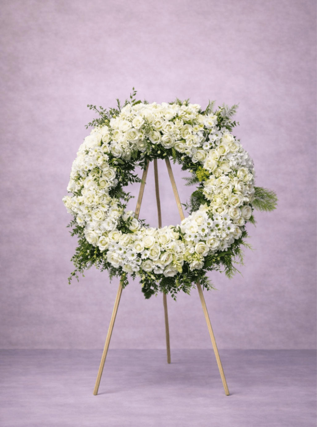 Large white floral wreath displayed on a wooden easel against a soft lavender background